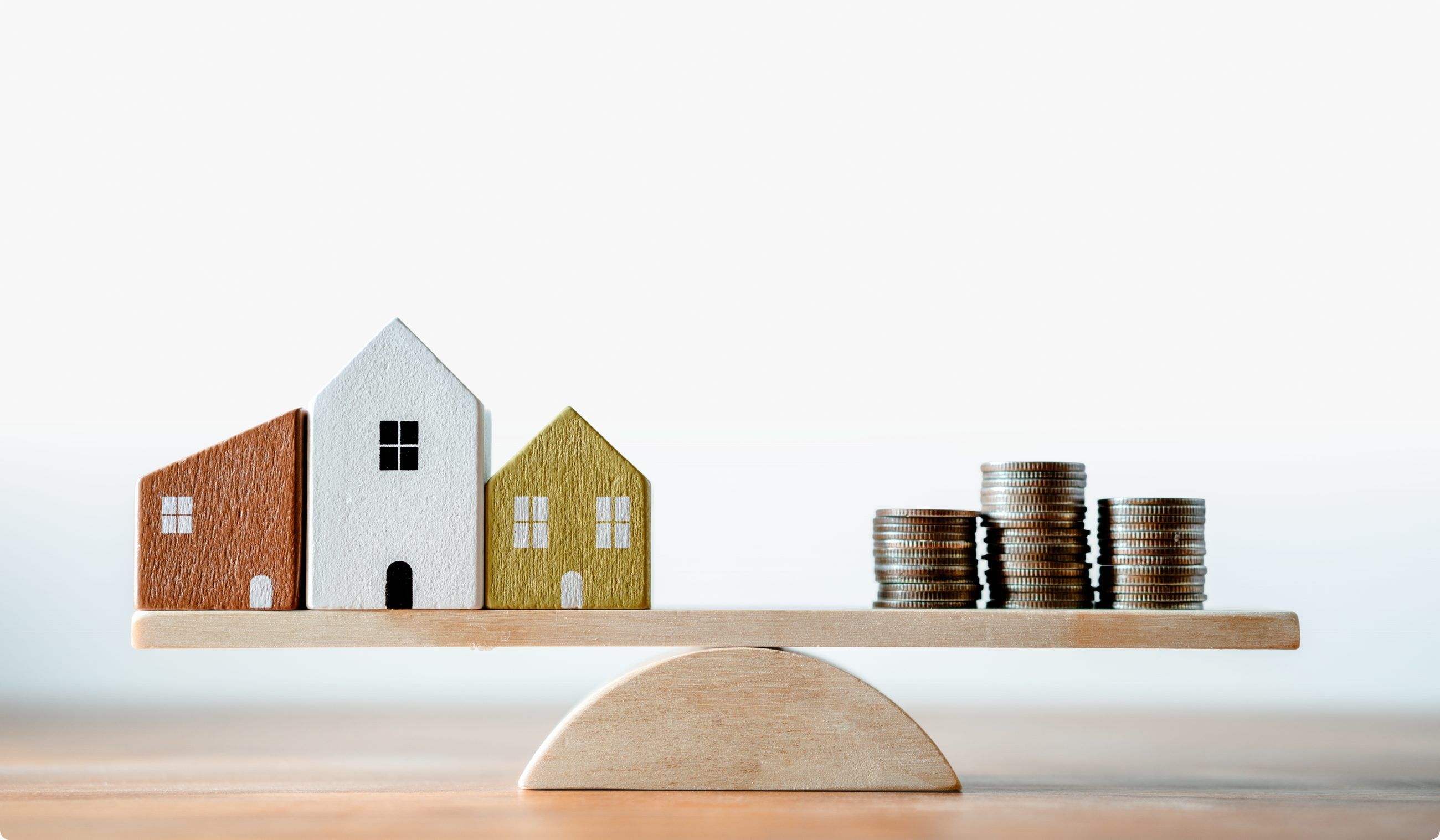 Wooden toy houses balanced against stacks of coins on a seesaw